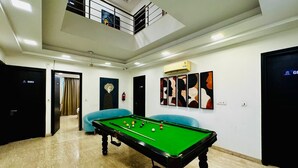 A pool table in a room with a high ceiling, a staircase, and a door marked 'G002'. - the royal oak sec 40 hotel gurgaon (Gurugram)