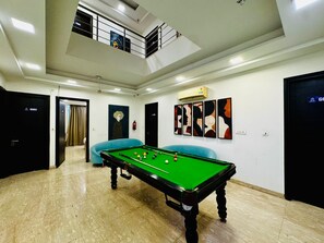 A pool table in a room with a high ceiling, a staircase, and a door marked 'G002'. - the royal oak sec 40 hotel gurgaon (Gurugram)