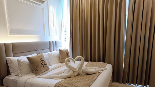 A hotel room with a bed, pillows, a quilted blanket, a bedside table, and a window with curtains. - the royal oak sec 40 hotel gurgaon (Gurugram)