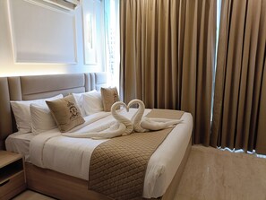 Habitación de hotel con cama, almohadas, manta acolchada, mesita de noche y ventana con cortinas.