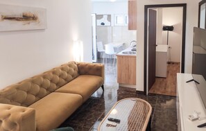 A modern living room with a tufted sofa, a glass coffee table, and a kitchen area visible through an open door. - 2 bedroom nice apartment in Okrug Gornji (Okrug Gornji)