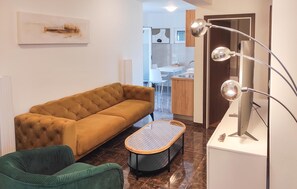 A modern living room with a sofa, a green chair, a small table, and a kitchen in the background. - 2 bedroom nice apartment in Okrug Gornji (Okrug Gornji)