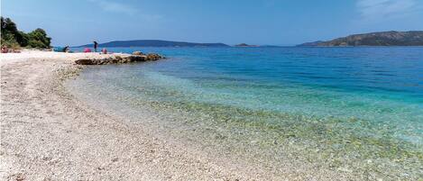 A pebble beach with clear water and distant mountains.