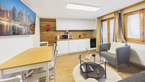 Une pièce moderne comprenant une table à manger, un canapé, un coin cuisine et une grande fenêtre avec des rideaux.