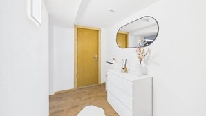Un couloir avec une commode blanche, un miroir et une porte en bois.