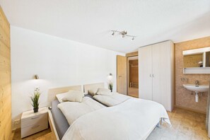 Ein Schlafzimmer mit Bett, Nachttischen, einem Spiegel und einem Badezimmer mit Waschbecken.