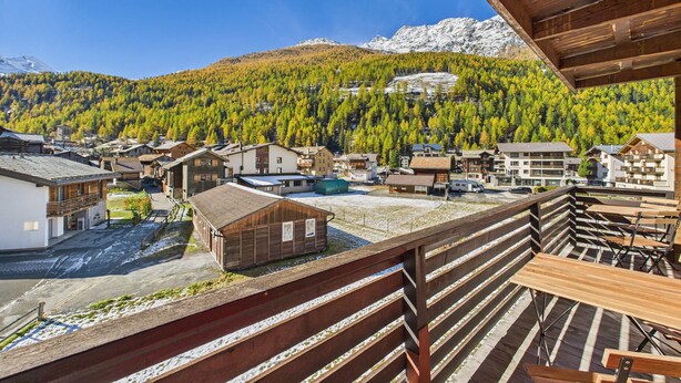 Ein Bergdorf mit Holzbauten, einer Holzterrasse und Blick auf schneebedeckte Berge.