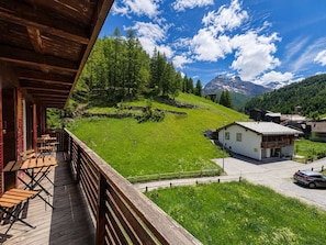 A wooden deck with chairs, a white building, and a mountain view.