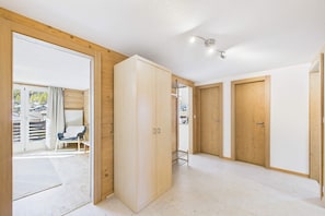 A room with a wooden wardrobe, a chair, and a view through a glass door.