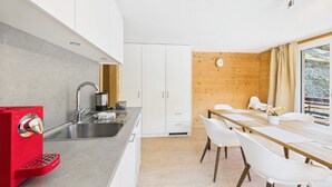 Eine moderne Küche mit weißen Schränken, einem roten Gerät und einem Essbereich mit Holztisch und weißen Stühlen.