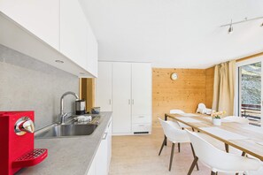 Eine moderne Küche mit weißen Schränken, einem roten Gerät und einem Essbereich mit Holztisch und weißen Stühlen.