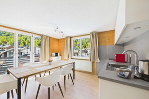 Eine moderne Küche mit Essbereich, großen Fenstern und Blick auf ein bewaldetes Gebiet.