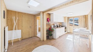 A modern kitchen with wooden walls, a dining area with a white table and chairs, and a view of a snowy landscape through a window.