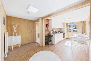 Una cocina moderna con paredes de madera, un comedor con una mesa y sillas blancas, y vistas a un paisaje nevado a través de una ventana.