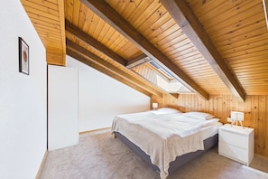 Ein Schlafzimmer mit schrägen Wänden, einem Bett, Nachttischen und einem weißen Kleiderschrank.