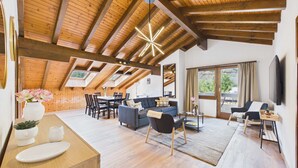 Un vaste loft doté de poutres apparentes, d’un coin repas, d’un salon avec des canapés et d’un téléviseur fixé au mur.