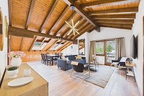Ein geräumiger Loft mit Holzbalken, einem Essbereich, einem Wohnzimmer mit Sofas und einem an der Wand montierten Fernseher.