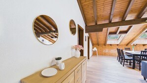 Un plafond en bois avec des poutres apparentes, une table à manger en bois avec des chaises, et un mur blanc orné de miroirs ronds.