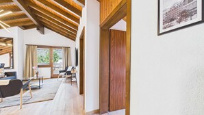 Une pièce spacieuse avec des poutres en bois, une grande fenêtre, une porte et un tableau encadré au mur.