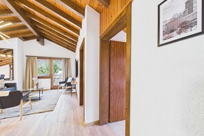 Quarto espaçoso com vigas de madeira, uma janela grande, uma porta e um quadro emoldurado na parede.