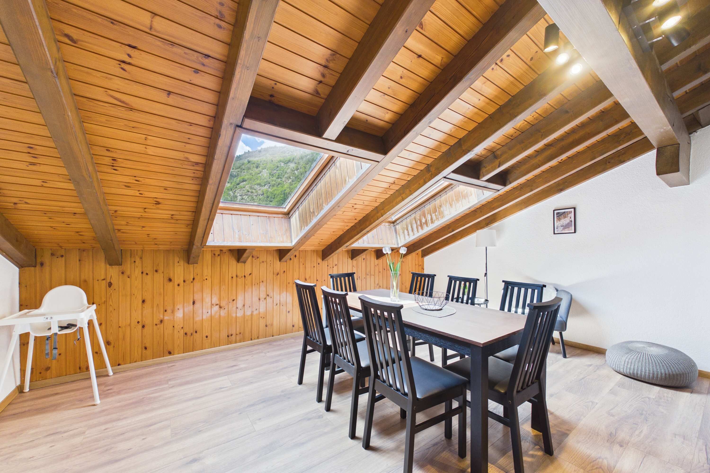 Un espace repas doté d’un plafond en bois, d’une table, de chaises et offrant une vue à travers une lucarne.
