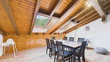 Un espace repas doté d’un plafond en bois, d’une table, de chaises et offrant une vue à travers une lucarne.