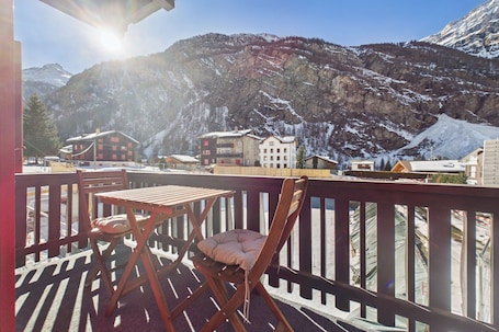 A balcony with a table and chair, overlooking a mountainous landscape with buildings.