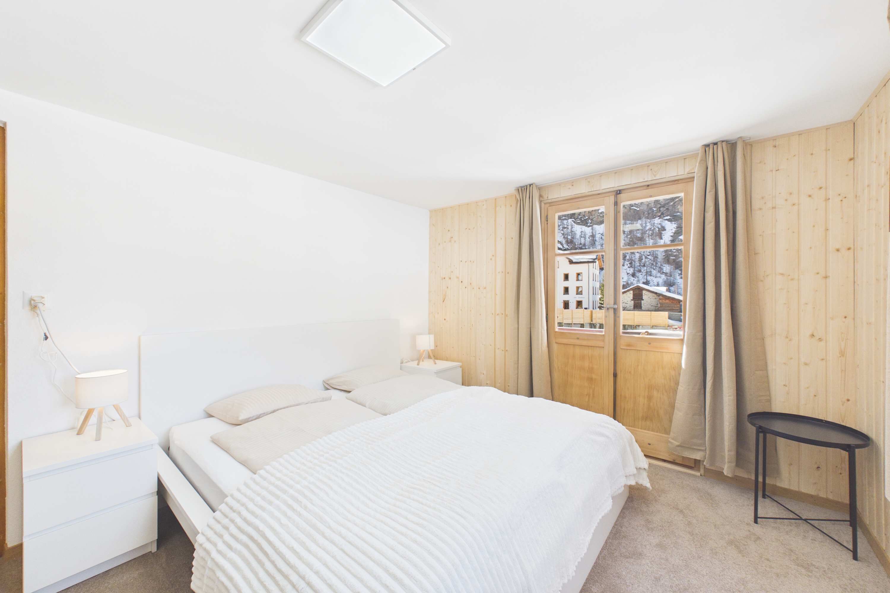 Un dormitorio con cama, mesitas de noche, una ventana con cortinas y vistas a un paisaje nevado.