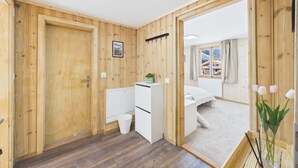 A room with wooden walls, a bed, a desk, a small white cabinet, a window with curtains, and a skylight.