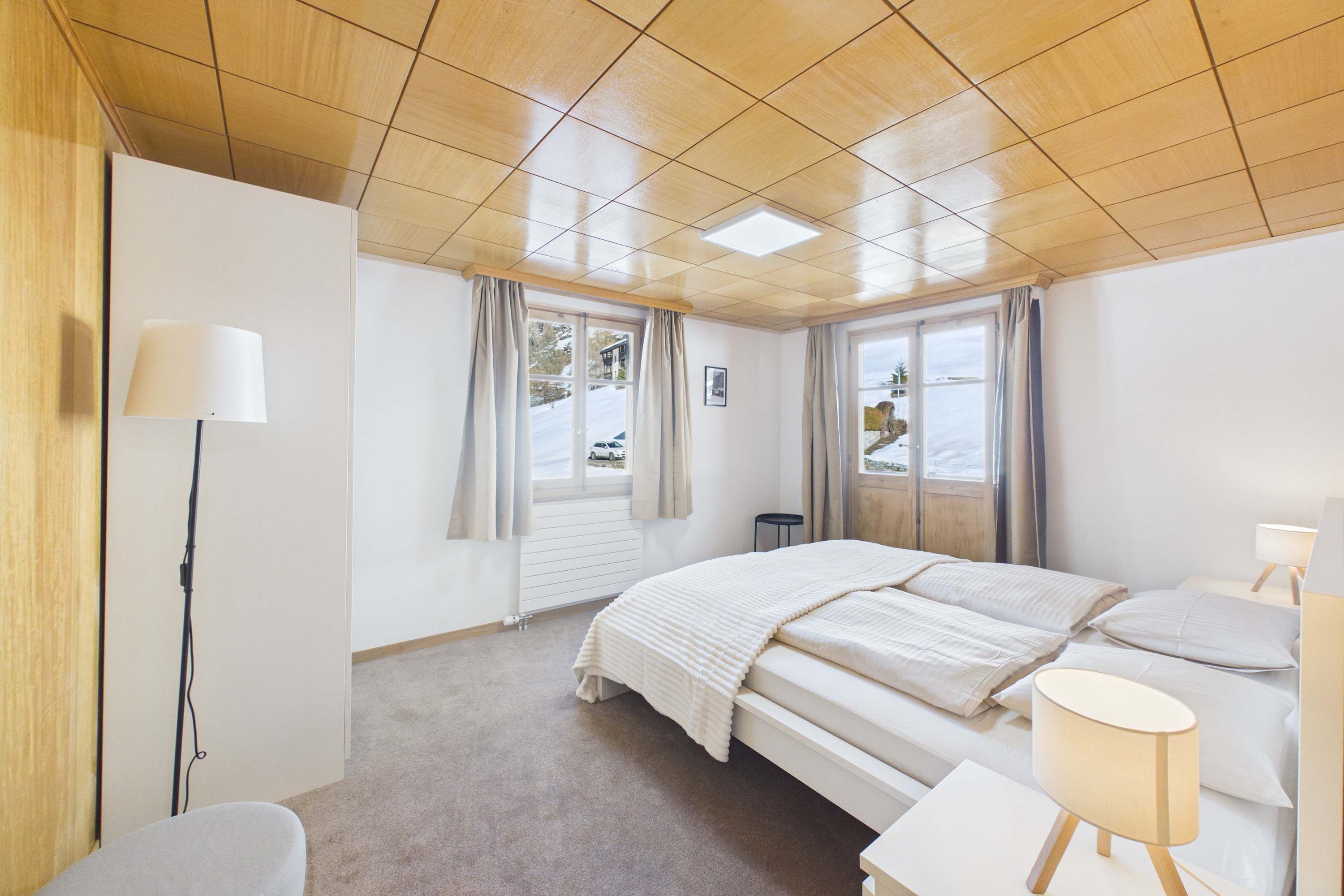 Een slaapkamer met een bed, nachtkastjes, een lamp, een stoel en een raam met gordijnen.
