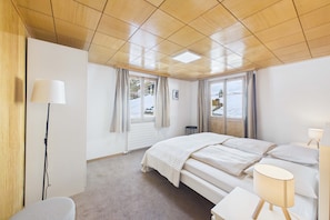 Ein Schlafzimmer mit Bett, Nachttischen, einer Lampe, einem Sessel und einem Fenster mit Vorhängen.