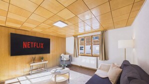 A modern living room with a large flat-screen TV, a sofa, a coffee table, and a window with curtains.