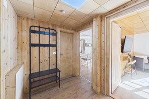 Un interior de madera con un banco, una puerta que da a un área exterior y un televisor sobre una pequeña mesa.