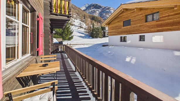 A wooden building with a balcony overlooking a snowy landscape and mountains.