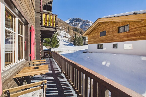 A wooden building with a balcony overlooking a snowy landscape and mountains.