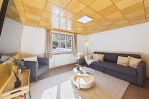 A modern living room with a wooden ceiling, a grey sofa, a round coffee table, and a window with curtains.
