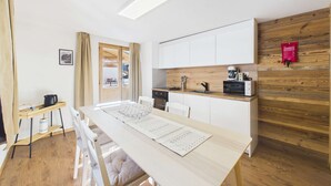 A modern kitchen with white cabinets, a wooden accent wall, a dining table with a menu, and a coffee machine.