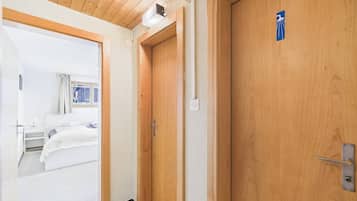 A hotel room with a wooden door, a bed, a bedside table, and a window with curtains.