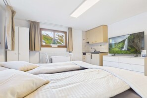 Slaapkamer met twee bedden, een televisie, een raam met gordijnen, een radiator en een kitchenette.