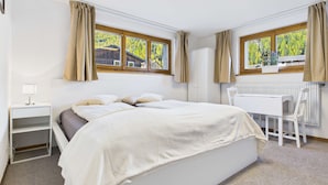 A bedroom with a bed, bedside table, chair, desk, and windows with curtains. - Mountain View Studio Near Saas-Fee Gondola (Saas-Grund)