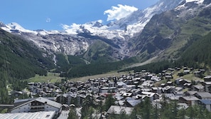 Un village de montagne aux maisons traditionnelles, une vallée et des sommets enneigés.
