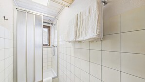 A bathroom with white tiled walls, a shower with a glass door, and a towel hanging on the wall. - Mountain View Studio Near Saas-Fee Gondola (Saas-Grund)