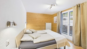 Une chambre à coucher avec une tête de lit en bois, un lit avec des oreillers, un luminaire fixé au mur et une fenêtre avec des rideaux.