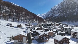 A snow-covered village with traditional wooden houses, a church, and mountains in the background.