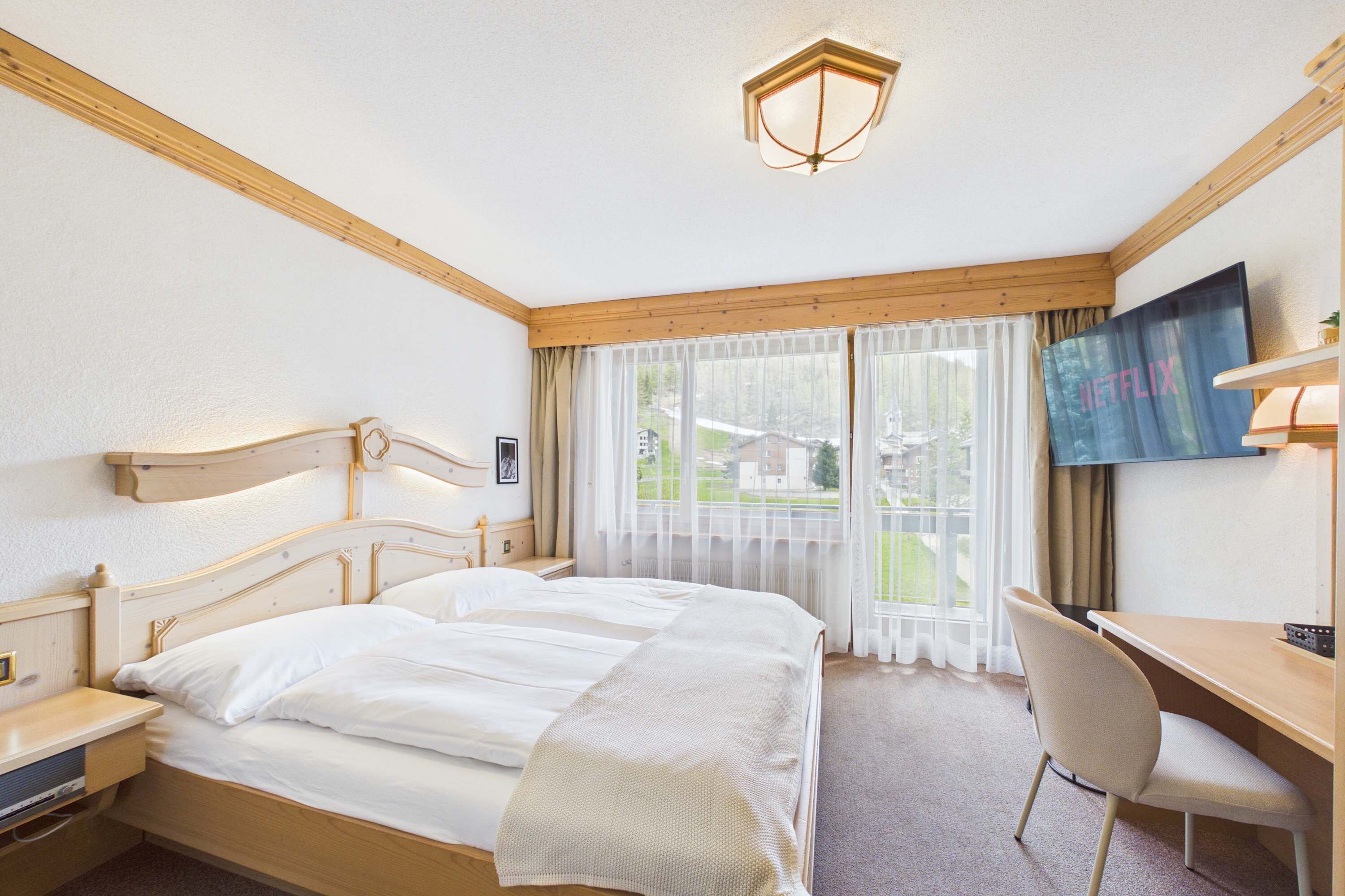 Une chambre d’hôtel avec un lit double, un bureau, une chaise, une télévision et une fenêtre avec des rideaux.