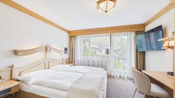 Une chambre d’hôtel avec un lit double, un bureau, une chaise, une télévision et une fenêtre avec des rideaux.