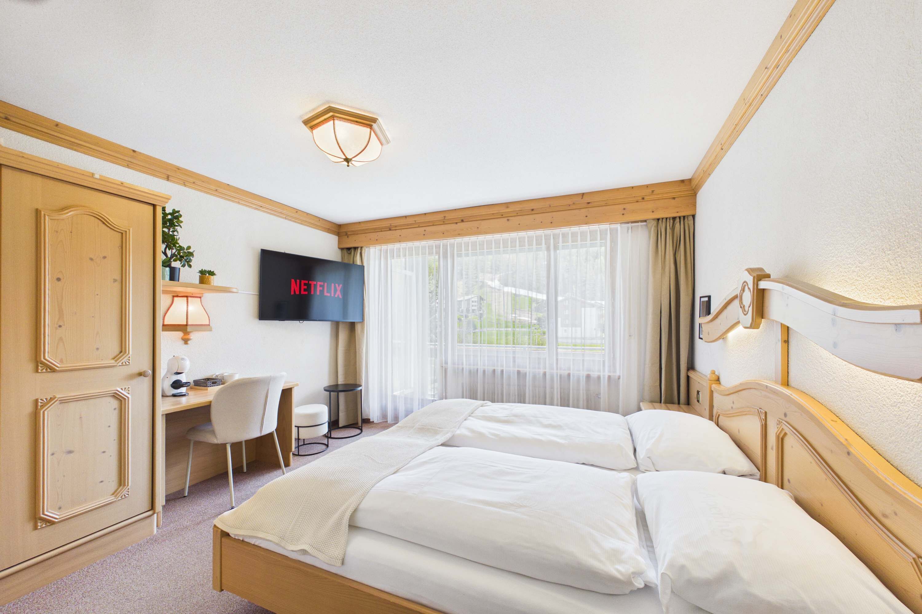 Een hotelkamer met een bed, bureau, stoel, televisie en een raam met gordijnen.