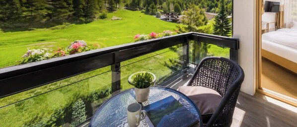 A balcony with a glass railing, a round table with a potted plant, a chair, and a bed with a TV. - Mountain View Suite + Self Check-in near SaasFee (Saas-Almagell)