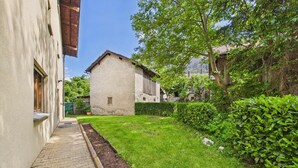 Un patio con un camino empedrado, un área verde y un edificio con una puerta de madera.