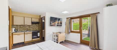 A compact room with a bed, a kitchenette, a dining area, and a window with curtains.